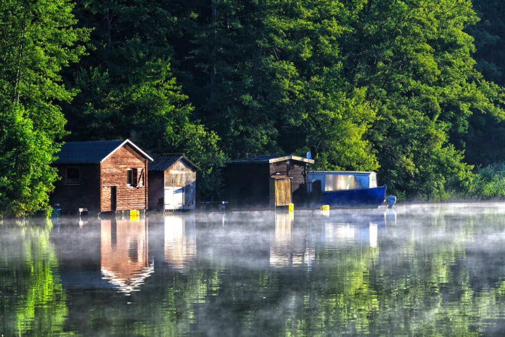 Bootshäuser am Ufer im sommerlichen Morgennebel