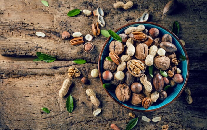 Verschiedene Nüsse geschält und in Schale in einer Schale auf einem groben Stück Holz