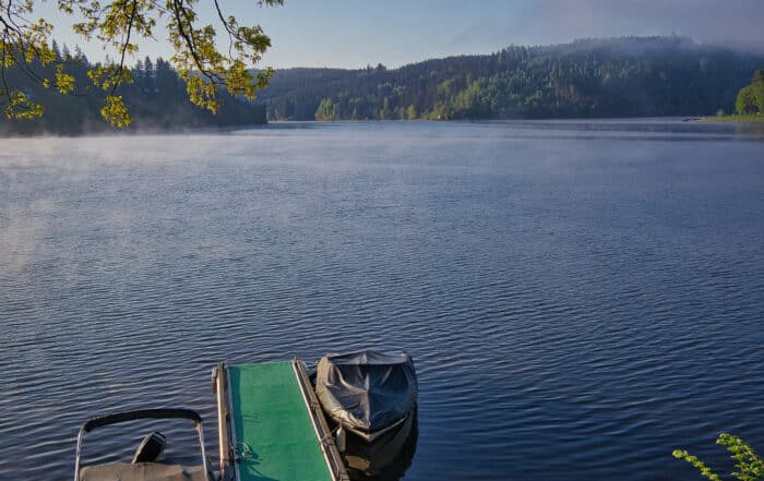 Blick auf den See am Morgen. Im Vordergrund Bootssteg mit 2 Booten.