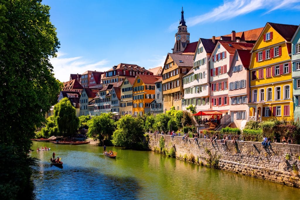 Altstadt von Tübingen im Sommer mit Stocherkähnen auf dem Neckar und Menschen, die auf der Mauer am Neckar in der Sonne sitzen