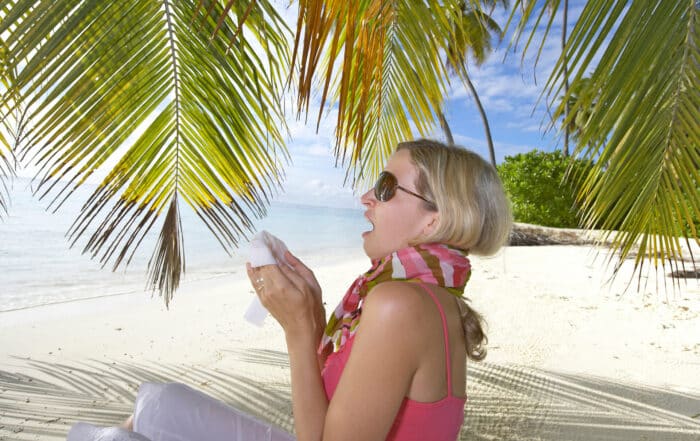 Blonde Frau am Strand unter Palmen mit Taschentuch niest