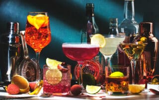 Verschiedene Cocktails, Flaschen und Barutensilien vor dunkelblauem Hintergrund