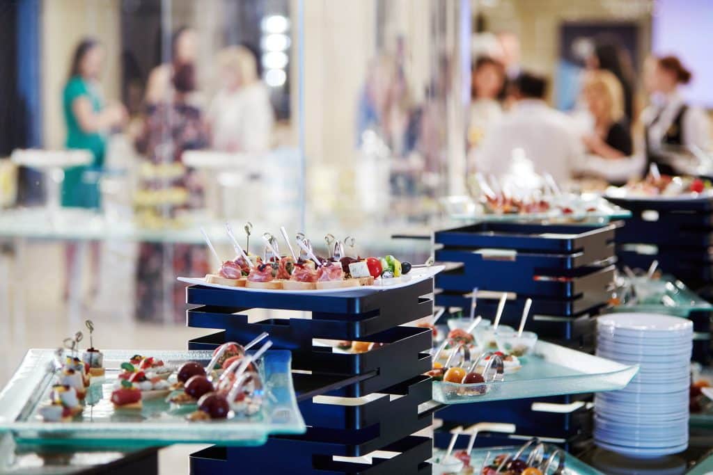Banquet table covered with trays with canapes with people standing in the background