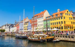 Sommer in Nyhavn in Kopenhagen. Viele Menschen sitzen an der kaimauer oder in Cafés und Restaurants.