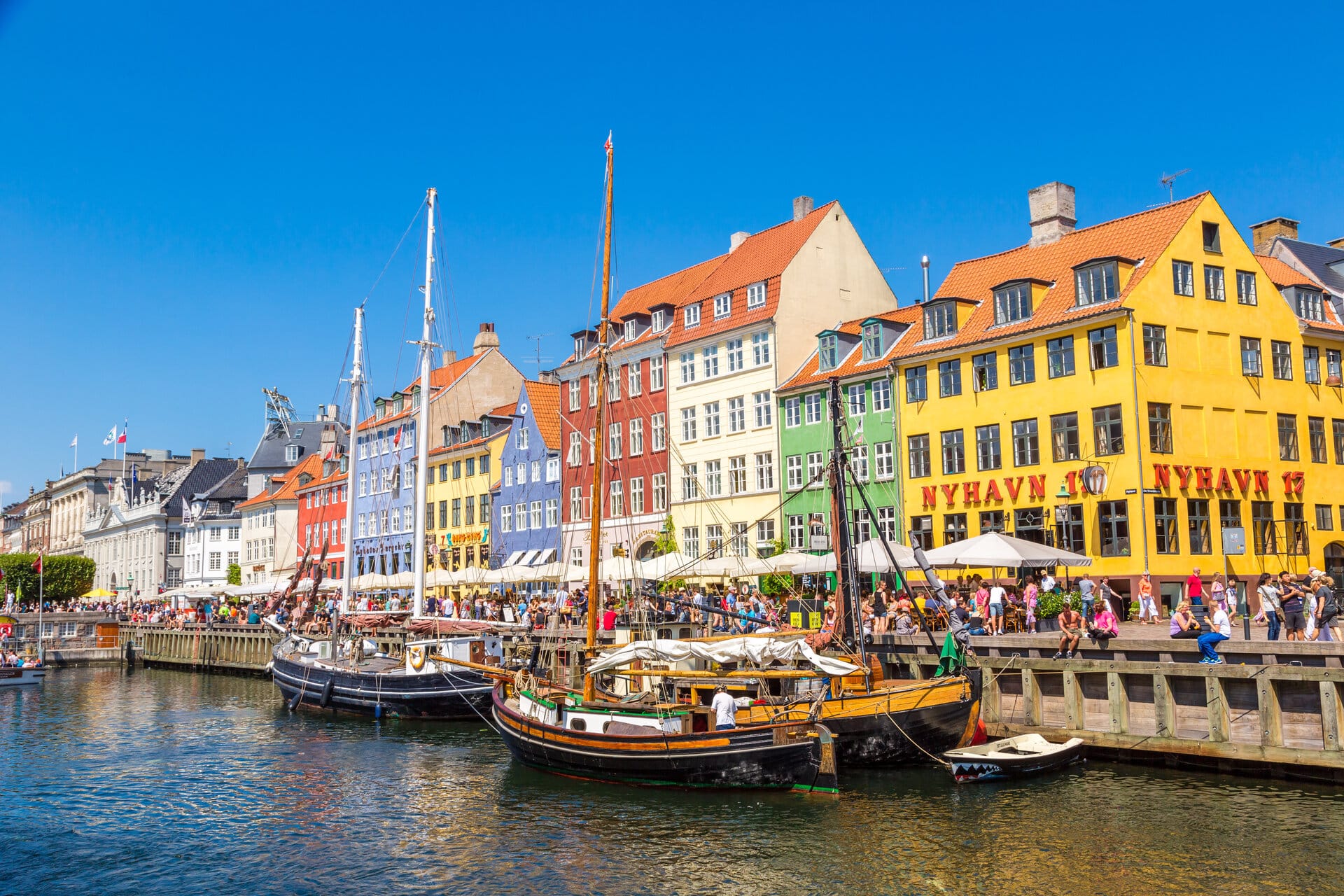 Sommer in Nyhavn in Kopenhagen. Viele Menschen sitzen an der kaimauer oder in Cafés und Restaurants.