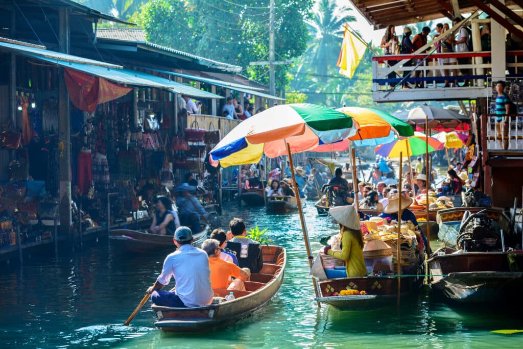 Boote mit Touristen und Einheimischen fahren durch einen floating Market in Thailand.