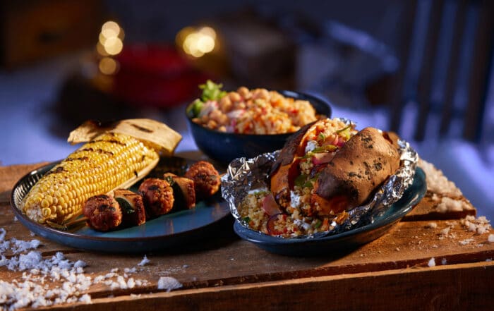Gegrilltes auf einen Holztisch mit Schneeflocken in einem Hof am Abend mit Lichtern iim Hintergrund
