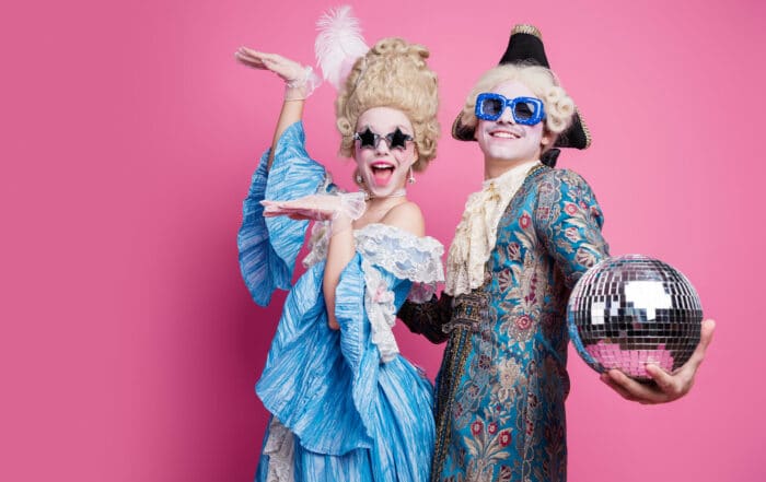 Energetic couple in baroque costumes poses joyfully against a vibrant pink background, capturing the essence of a themed carnival