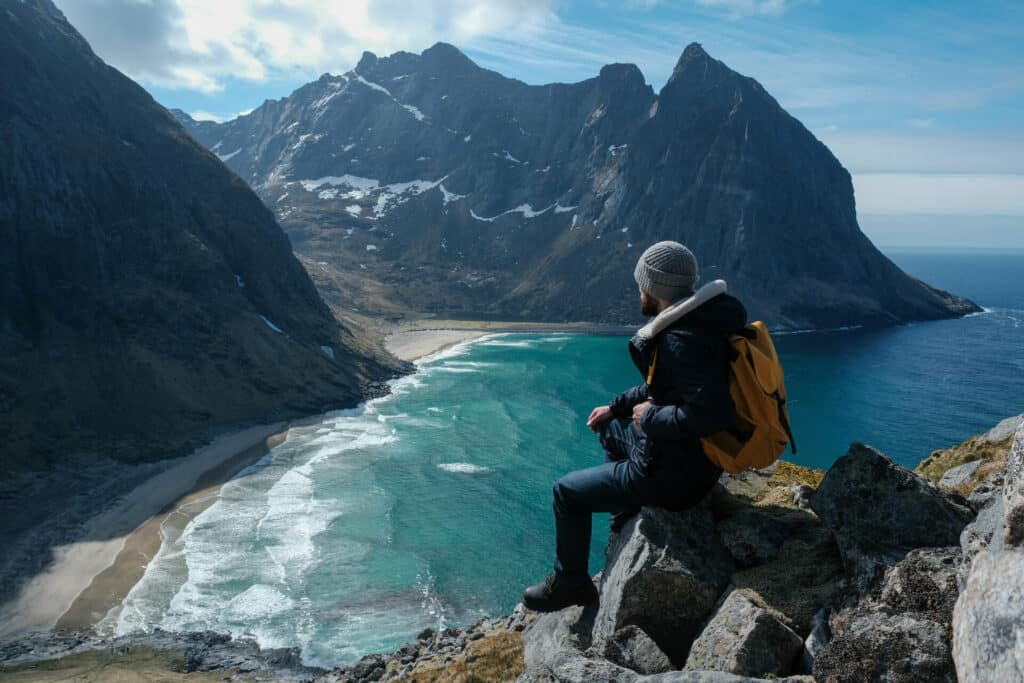 Mann sitzt auf einem Fels und blickt auf den Strand am Reinebringen Berg in Norwegen