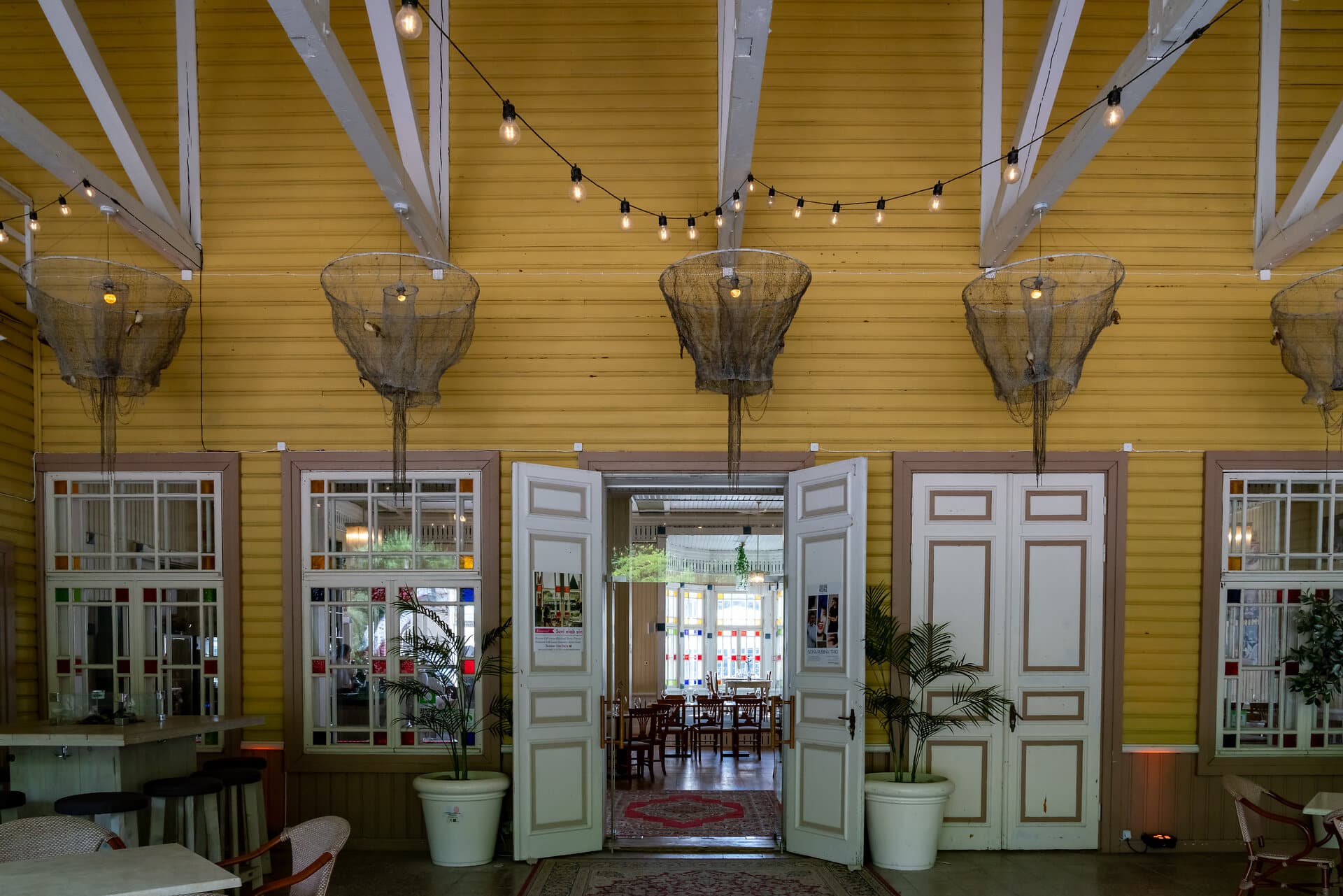 Blick in ein traditionelles Gasthaus auf Saaremaa in Estland, Haus aus gelben Holzplanken mit weißen Balken, Fensterrahmen und Kassettentüren, Lampen mit Fischernetzen.