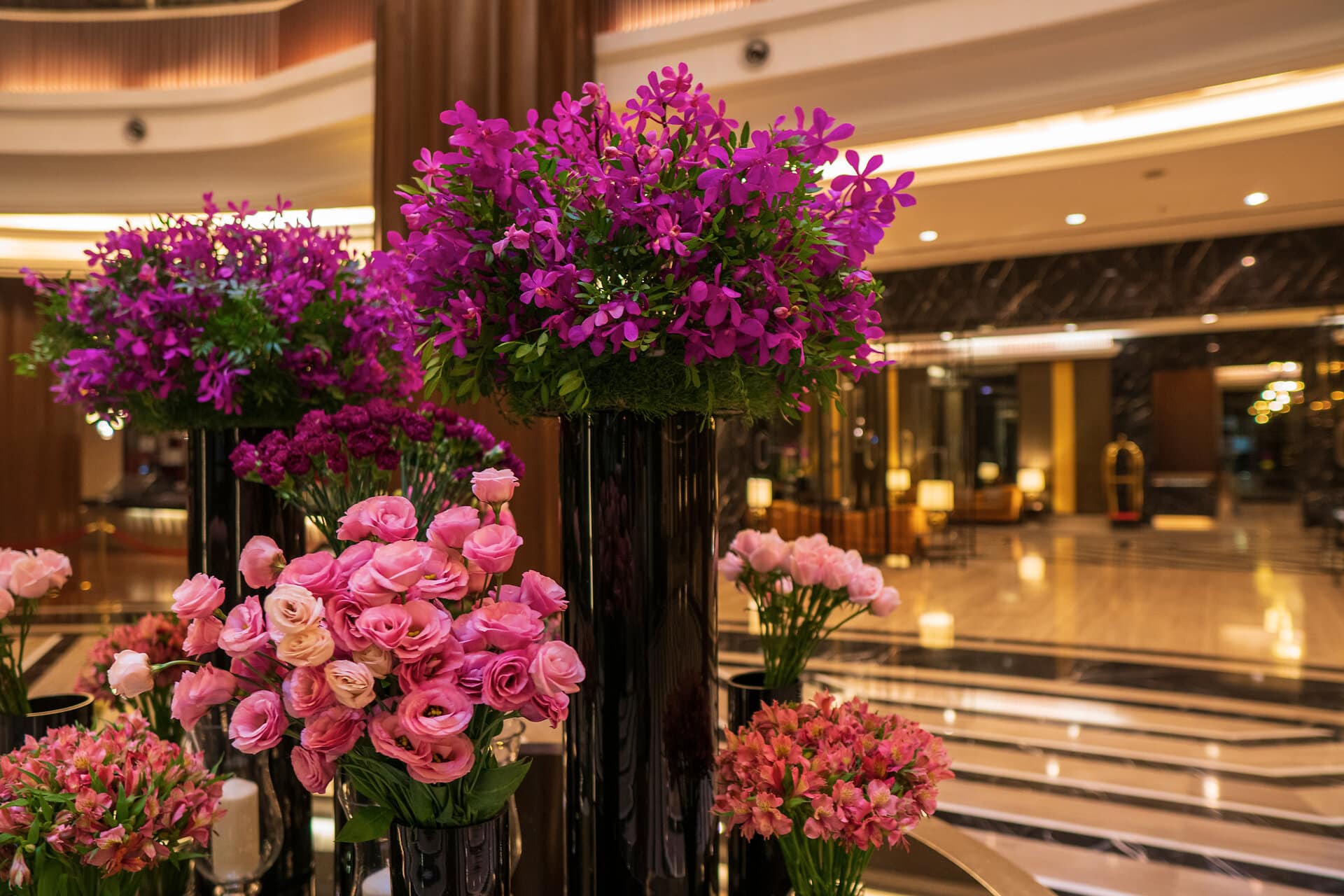 große dunkle Glasvasen in verschiedenen Größen in einer Hotellobby mit rosafarbenen Rosen, Fresien und Lilien