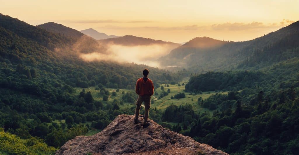 Man standing on top of cliff at sunset