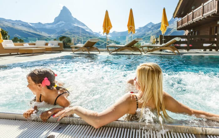 Frau und Kind im Outdoorpool eines Hotels im Alpenländischen Stil mit Blick auf markantes Bergpanorama