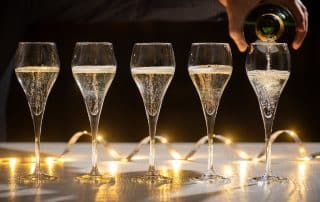 New year party, pouring of brut champagne bubbles cava or prosecco wine in tulip glasses with garland lights on background