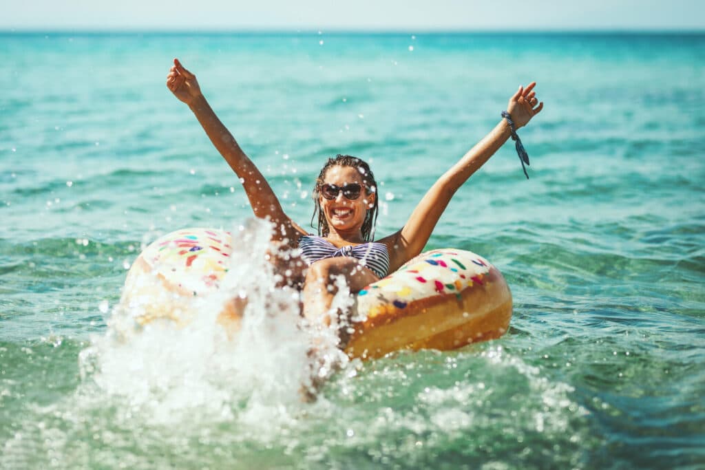 Junge Frau sitzt auf einem Schwimmriung im Meer und freut sich.