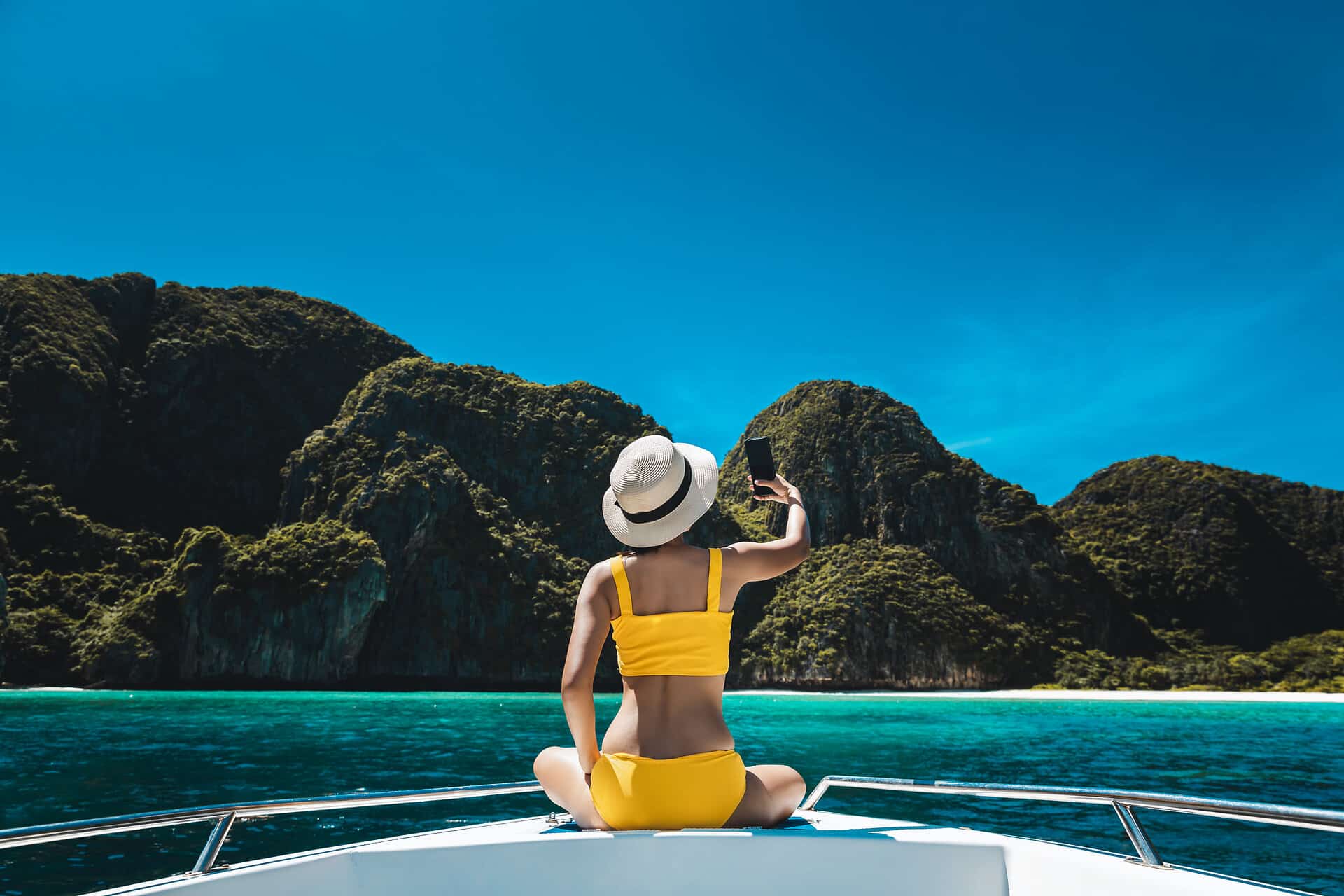 Traveler asian bikini woman with mobile phone travel on boat in Maya Bay Phuket Thailand
