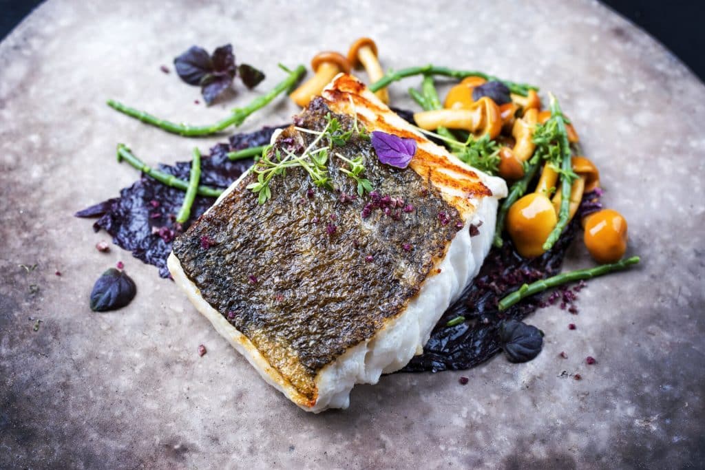 auf der Haug cross gebratenes Fischfilet mit Kräutern und Blüten angerichtet