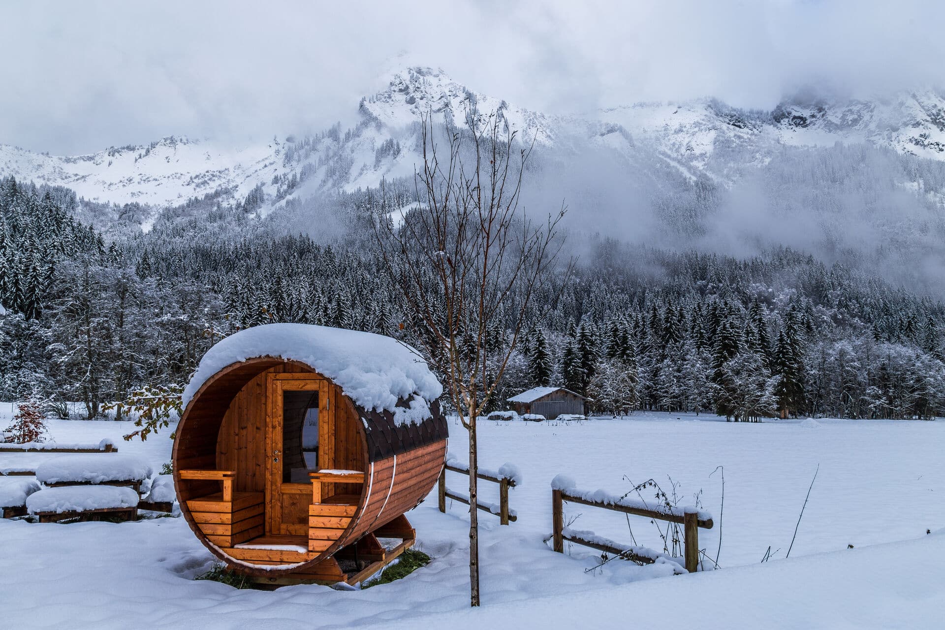 Fass-Sauna im Schnee mit Bergen im Hintergrund