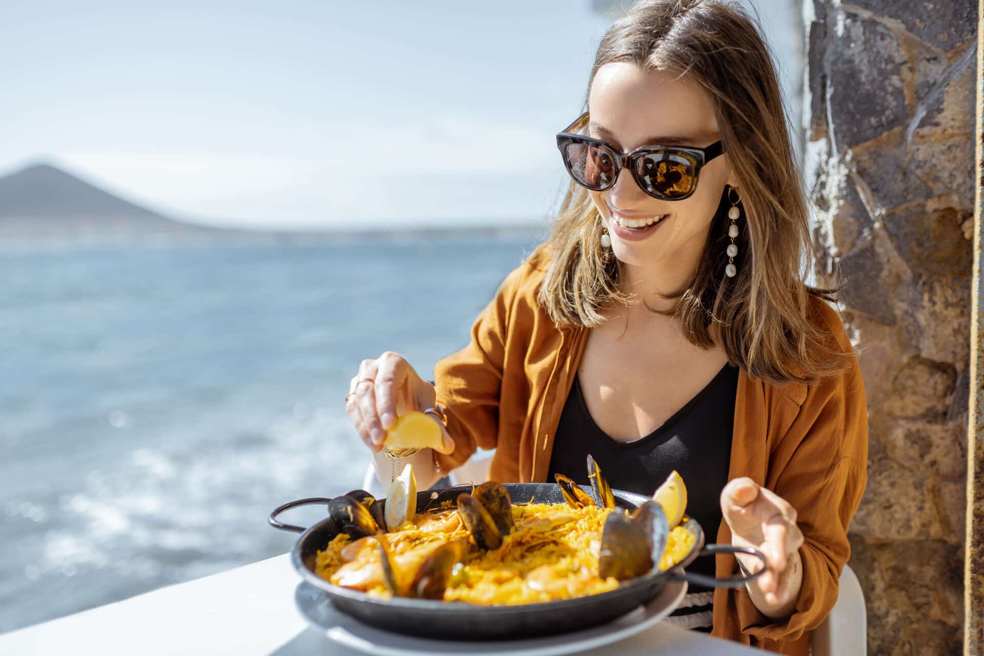 Frau ißt Paella in der Sonne am Meer