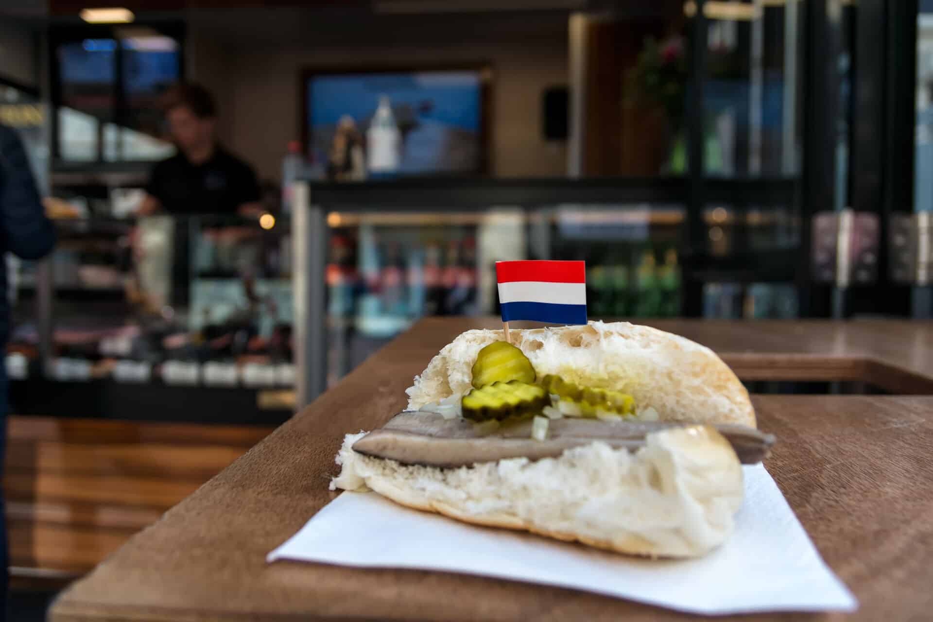 Traditional dutch snack, seafood sandwich with herring, onions and pickled cucumber. Broodje haring on the wooden table. With flag of Netherlands.