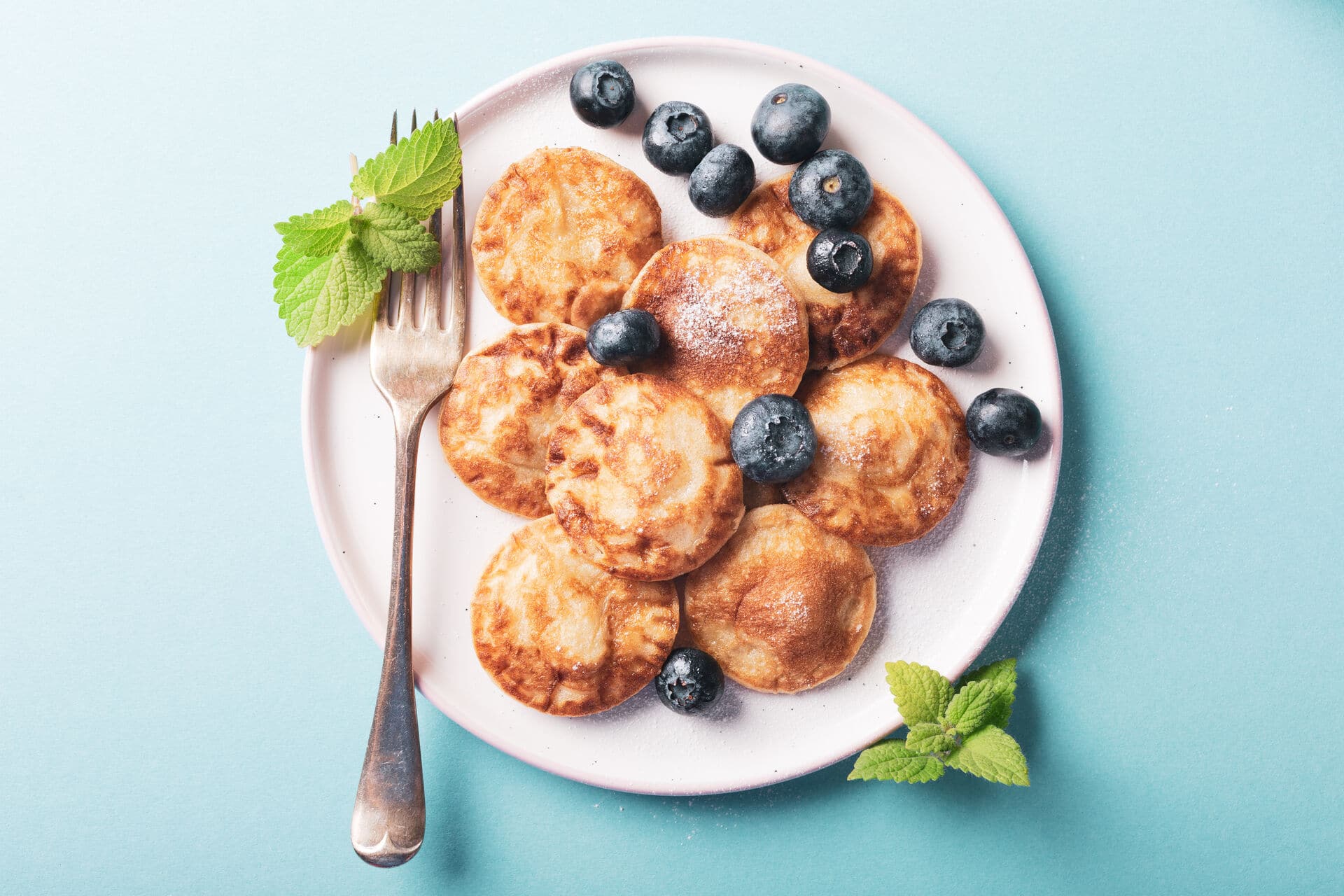 Overhead shoot of dutch mini pancakes called poffertjes with blueberries, sprinkled with powdered sugar. Healthy food concept with copy space.