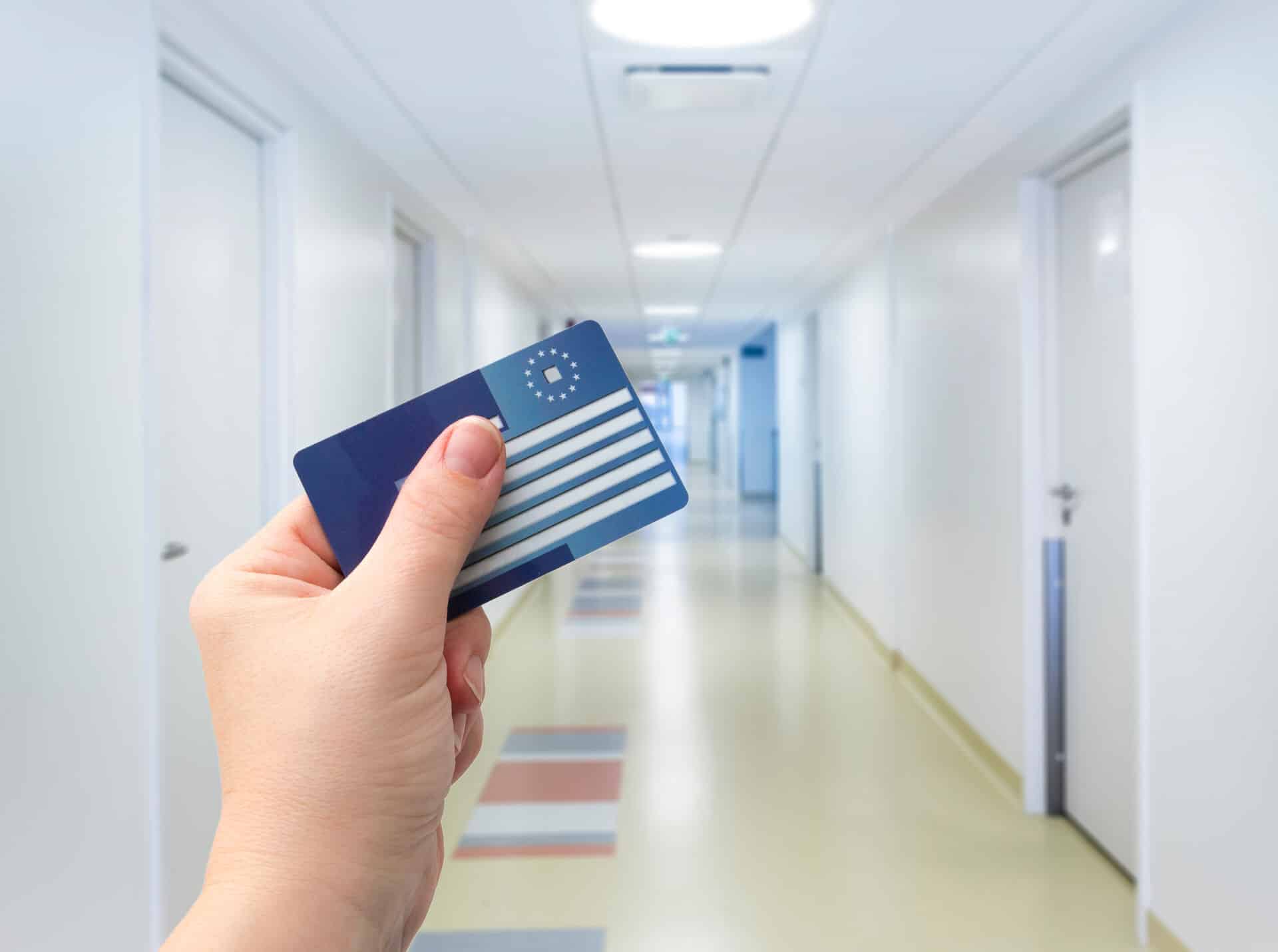 Hand hält Versichertenkarte im Krankenhausflur