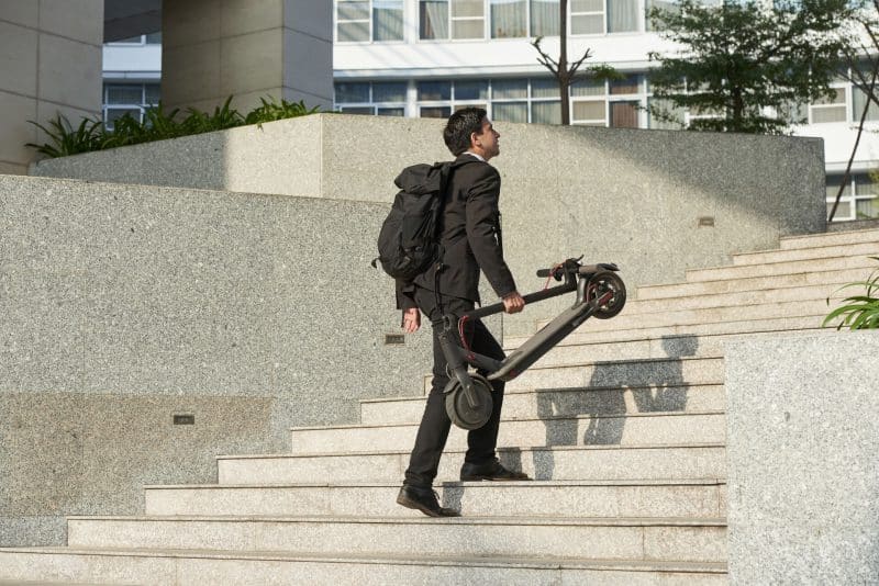 Mann läuft treppauf mit zusammengeklapptem Scooter