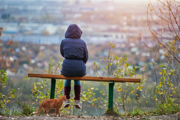 Junge Frau im Anorak auf einer Bank mit Blick auf die herbstliche Stadt